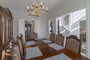 Ein Esszimmer mit Holztisch, sechs Stühlen, einer Chandelierleuchtre und Blick auf eine Treppe.