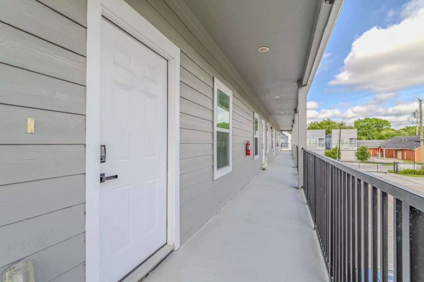 A covered porch with a white door, a fire extinguisher, and a view of the street.