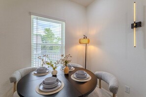A dining area with a round table, chairs, a vase with flowers, a floor lamp, and a window with blinds. - Cozy NRG apt for 5 near NRG stadium (Houston)