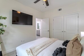 A bedroom with a bed, a TV mounted on the wall, a ceiling fan, and a door leading to a bathroom. - Cozy NRG apt for 5 near NRG stadium (Houston)