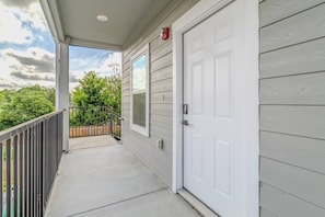 A covered porch with a white door, a metal railing, and a view of greenery. - Cozy NRG apt for 5 near NRG stadium (Houston)
