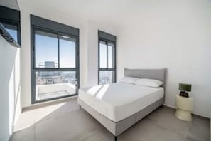Un dormitorio moderno con una cama grande, dos ventanas y vistas a la ciudad.