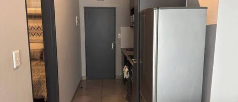 A narrow hallway with a door at the end, a refrigerator, and a small kitchen area with a sink and towel rack.