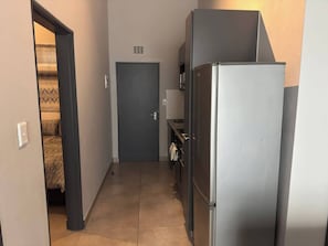 Ein schmaler Flur mit einer Tür am Ende, einem Kühlschrank und einer kleinen Küchenzeile mit Spüle und Handtuchhalter.