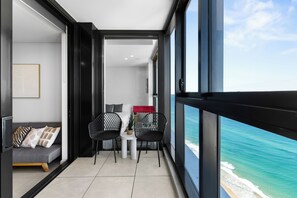Ein Balkon mit Blick auf das Meer, eine Couch, zwei Stühle und ein kleiner Tisch.