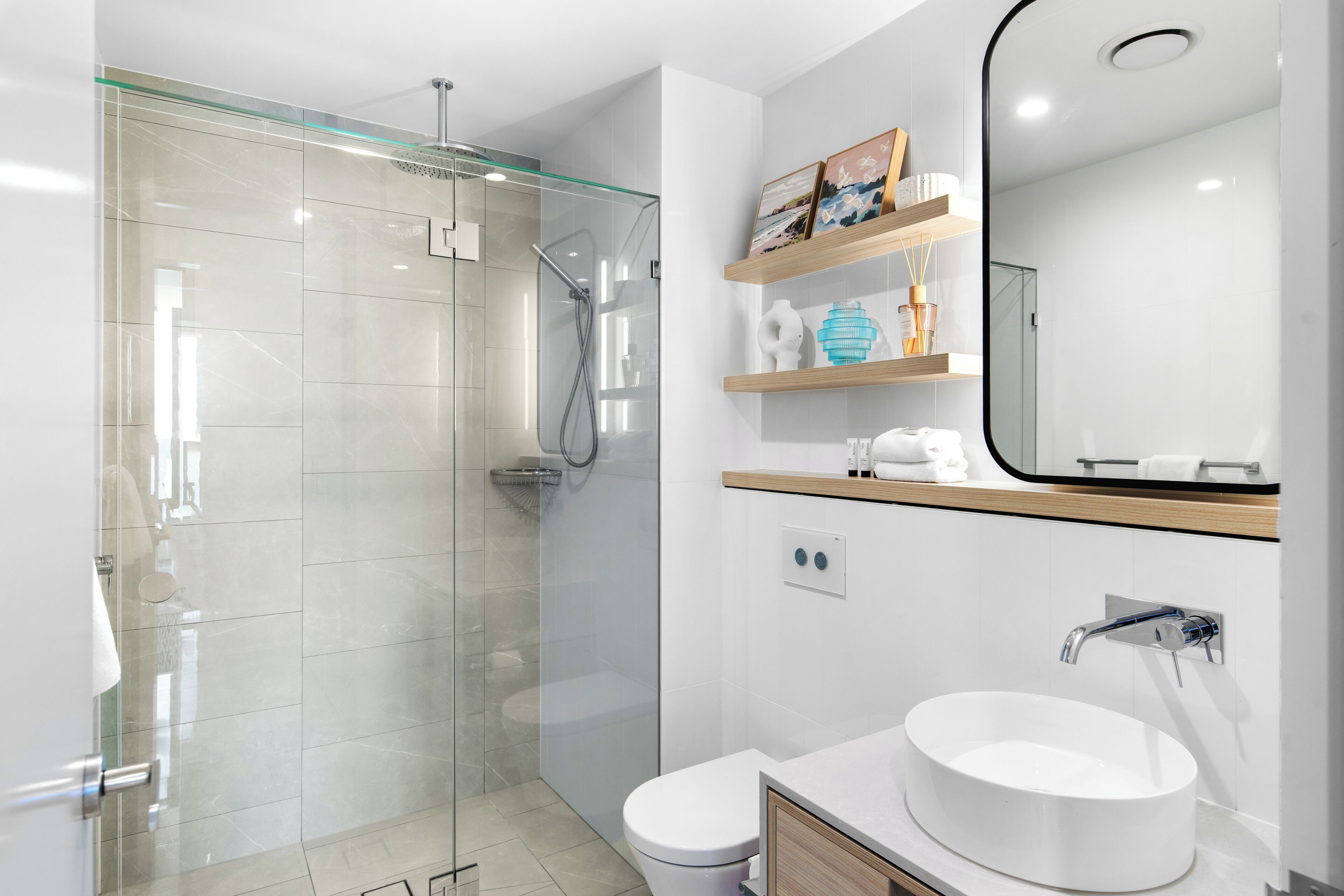 Un baño moderno con ducha de vidrio, un lavabo blanco y un espejo sobre el mueble.