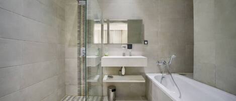 Un baño moderno con cabina de ducha de vidrio, un lavamanos blanco, un espejo y una bañera.