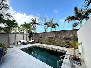 A swimming pool with a stone wall, lounge chairs, and potted plants. - Modern Villa Nestled in its Tropical Garden (Grand-Baie)