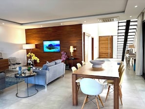 A modern living room with a sofa, coffee table, TV, and a dining area with chairs and a table. - Modern Villa Nestled in its Tropical Garden (Grand-Baie)