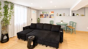 A living room with a sectional sofa, a small round table, and chairs. There is a plant on the left and artwork on the walls. - Cozy Seattle Suite Near SeaTac Airport & Downtown Seattle (Burien)