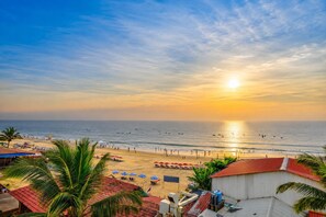 A beach view with a sunset, palm trees, and beach umbrellas. - Hotel Salty Waves Baga (Calangute)