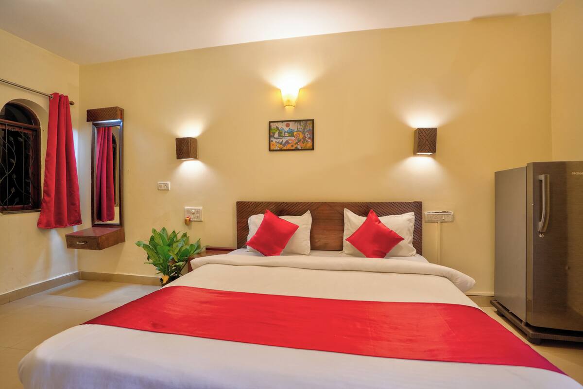 Una habitación de hotel con una cama, un refrigerador, una lámpara en la pared y un cuadro.
