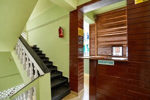 A staircase with a wooden handrail, a reception desk, and a fire extinguisher on the wall. - Hotel Salty Waves Baga (Calangute)