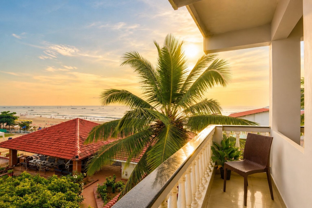 Een balkon met uitzicht op strand en zee, een palmboom en tuinmeubilair.