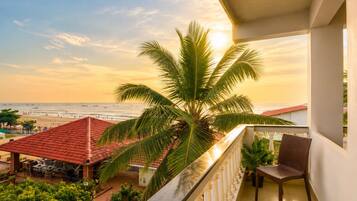 Un balcón con vista a la playa y al océano, una palmera y mobiliario exterior.
