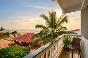 Een balkon met uitzicht op een strand, een palmboom en een gebouw met een rood dak.