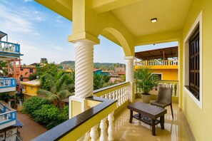 A balcony with a view of a residential area, a white column, a potted plant, and a wicker chair. - Hotel Salty Waves Baga (Calangute)