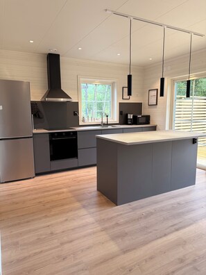 A modern kitchen with a central island, stainless steel appliances, and a large window providing natural light. - Sönnvik, NEW—right on the lake, sleeps 8, hot tub, sauna, dock, boat, barbecue area (Hultsfred)