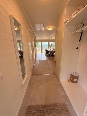 A hallway with a dining area at the end, a shoe rack, and a door leading to another room.