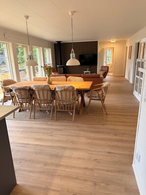A modern dining area with a wooden table and chairs, a large pendant light, and a television in the background. - Sönnvik, NEW—right on the lake, sleeps 8, hot tub, sauna, dock, boat, barbecue area (Hultsfred)
