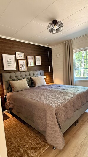 A bedroom with a tufted headboard, a patterned bedspread, framed motivational quotes on the wall, and a window with curtains. - Sönnvik, NEW—right on the lake, sleeps 8, hot tub, sauna, dock, boat, barbecue area (Hultsfred)