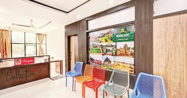 A reception area with a sign labeled 'Collection' and a 'Reception' sign, a reception desk, and colorful chairs in front of a wall displaying tourist attractions. - Hotel The Moon Light Inn Bhubaneswar (Bhubaneshwar)