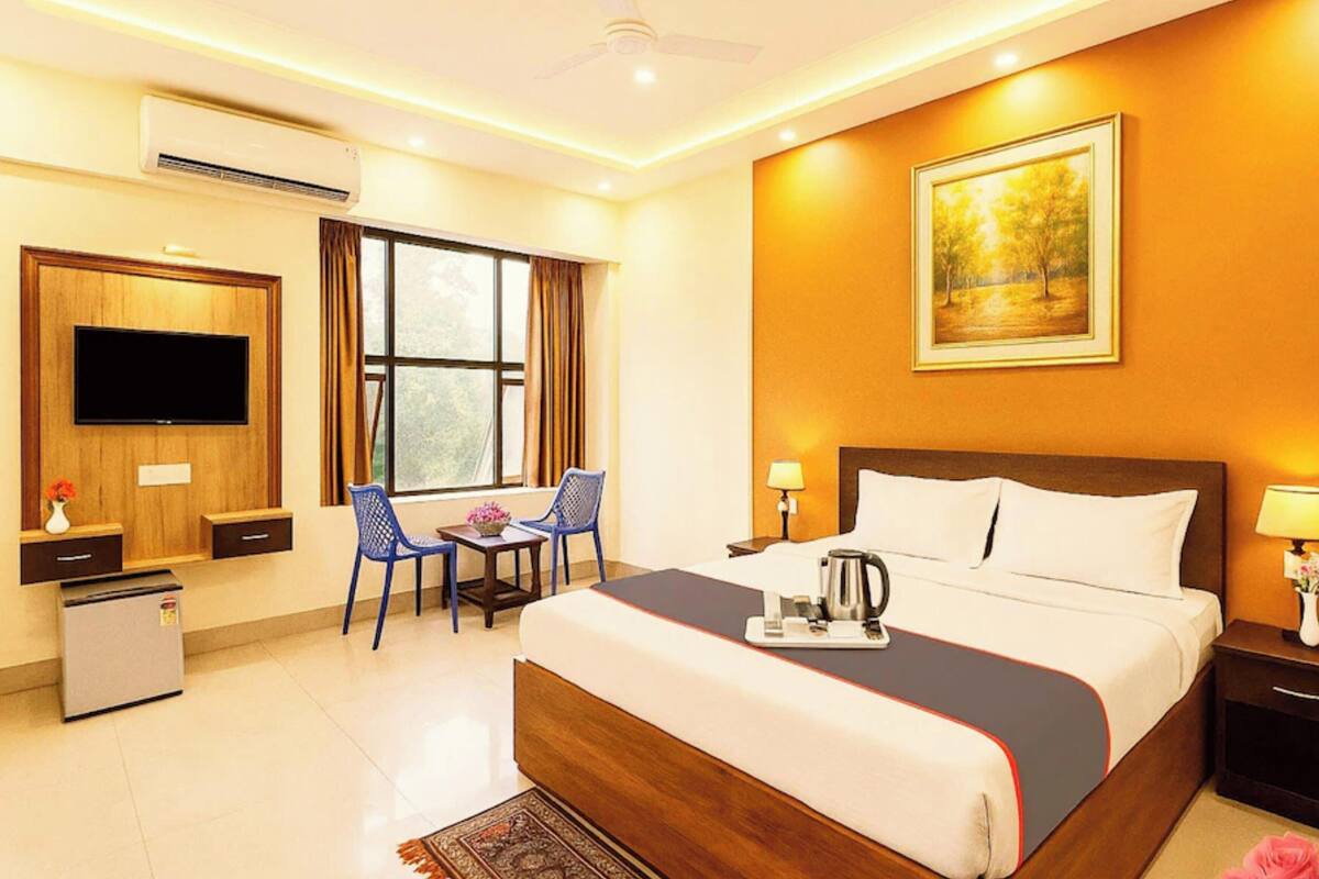 A hotel room with a bed, a desk, a TV, a window, and a painting on the wall.
