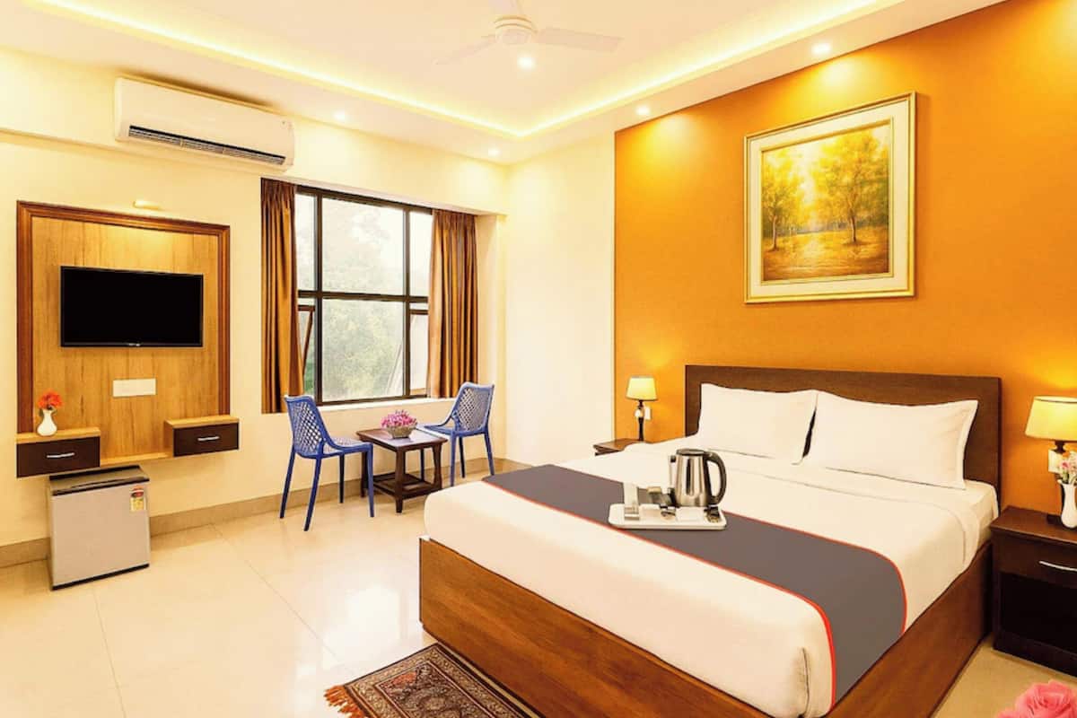 A hotel room with a bed, a desk, a TV, a window, and a painting on the wall.