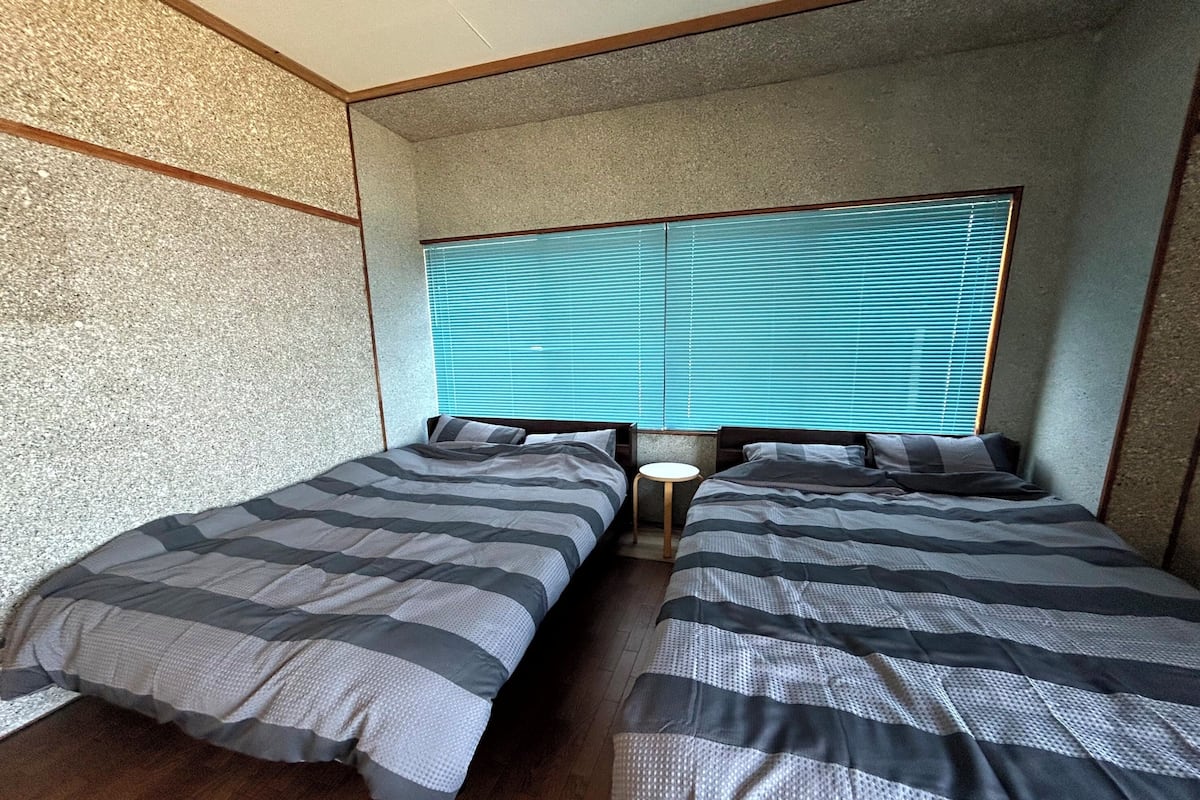 Une chambre avec deux lits, une petite table ronde et une fenêtre avec des stores.