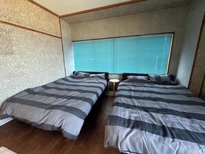 A room with two beds, a small round table, and a window with blinds. - MACARA Guesthouse (Nichinan)