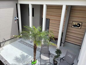 L’extérieur d’un hôtel, avec un palmier, des sièges en plein air et un mur en bois orné d’un tableau encadré.