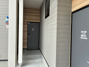 Een hotelentree met een modern ontwerp, met een donkere deur, een welkomstbord, een trap en een muur met een structuurpatroon.
