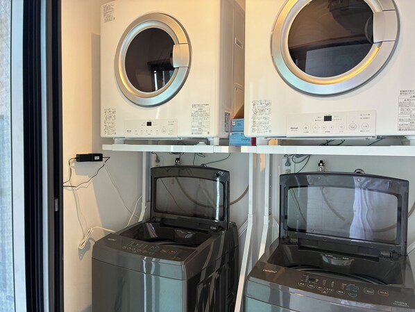 Une buanderie équipée de deux machines à laver à chargement frontal et de deux sèche-linge, avec des panneaux de commande et des manuels d’utilisation à portée de vue.