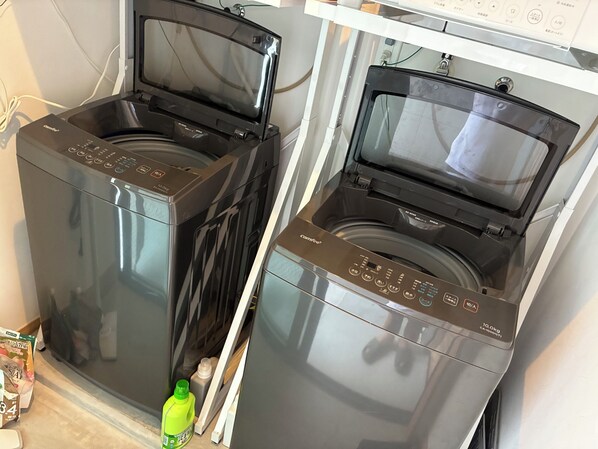 Two front-loading washing machines with a control panel, a green bottle, and a cardboard box on the floor.