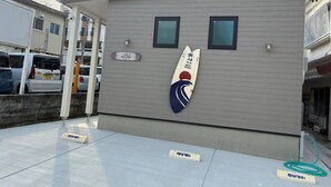 Un edificio con letrero que indica que es un hotel, una decoración con una tabla de surf y un área de estacionamiento con letrero.