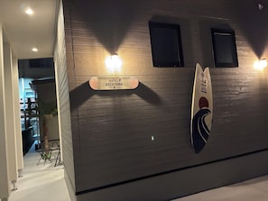Een houten wand met een bord voor Hotel Koza, een surfboard en twee wandlampen.