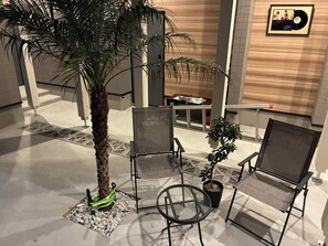 A hotel lobby with a palm tree, two chairs, a small table, and a framed picture on the wall.