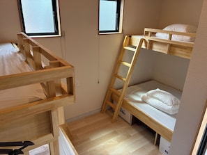 A bunk bed room with a wooden ladder, two windows, and a white mattress.
