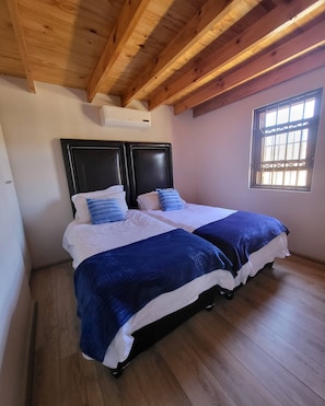 Un dormitorio con dos camas, suelo de madera, techo inclinado y una ventana con barrotes.