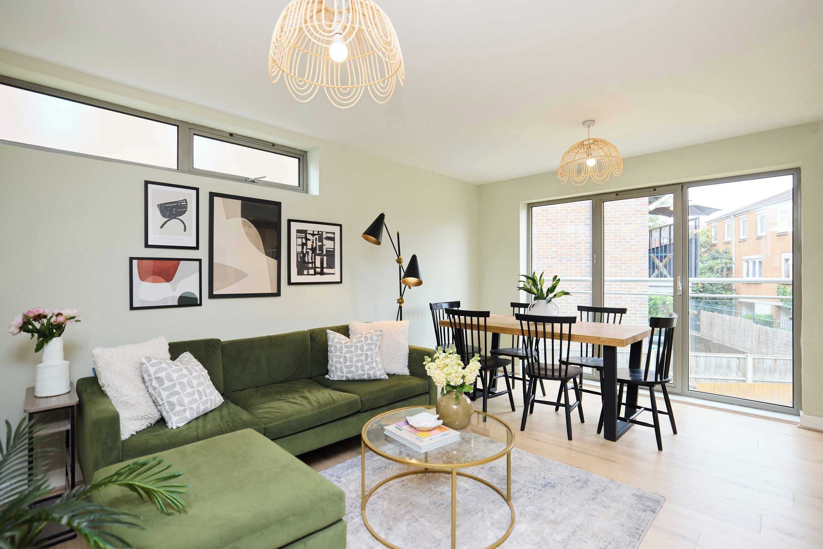 A modern living room with a green sofa, a dining table with chairs, and artwork on the walls.