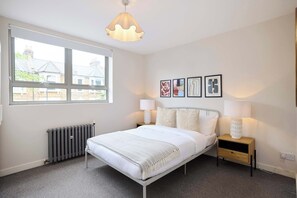 Ein Schlafzimmer mit Bett, Nachttischlampen, Heizkörper, Fenster und Wandbildern.