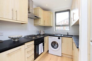 A compact kitchen with a washing machine, a stove, and a window. - Stoke Newington Olive Velvet Three-Bed (Greater London)