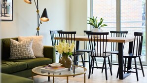 Ein Wohnzimmer mit einem grünen Sofa, einem runden Couchtisch, einem Esstisch mit Stühlen und einer Zimmerpflanze.