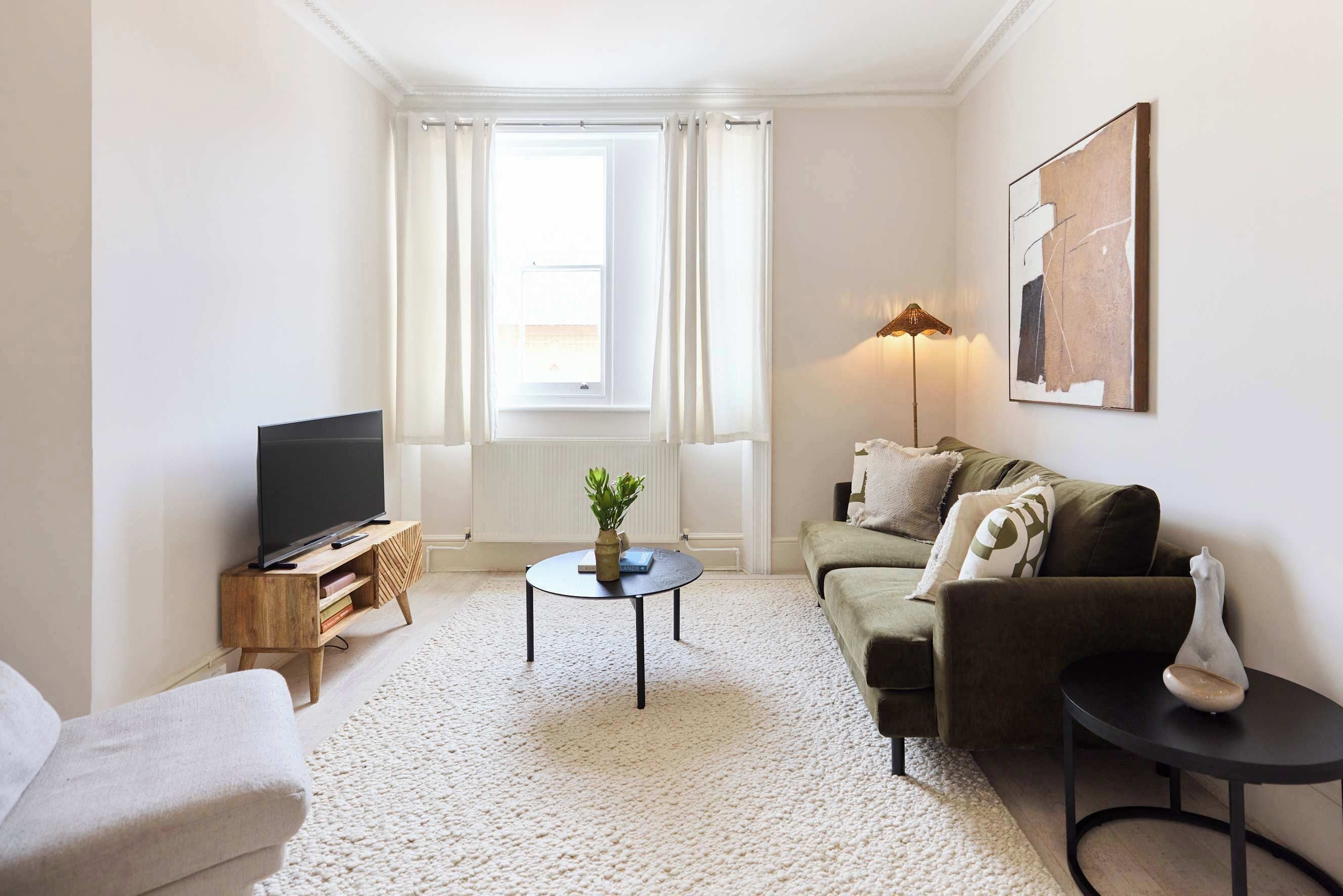 A living room with a flat-screen TV, a round coffee table, a sofa, a small side table, and a lamp.