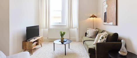A living room with a flat-screen TV, a round coffee table, a sofa, a small side table, and a lamp.