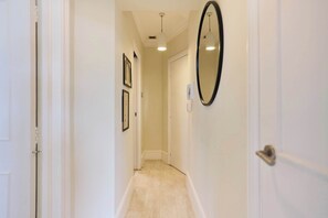 A narrow hallway with a light-colored floor, white walls, and a door at the end. - Olive Velvet & Marble - South Kensington (Greater London)