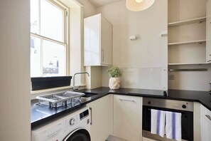 A compact kitchen with a washing machine, a sink, and a small oven. - Olive Velvet & Marble - South Kensington (Greater London)