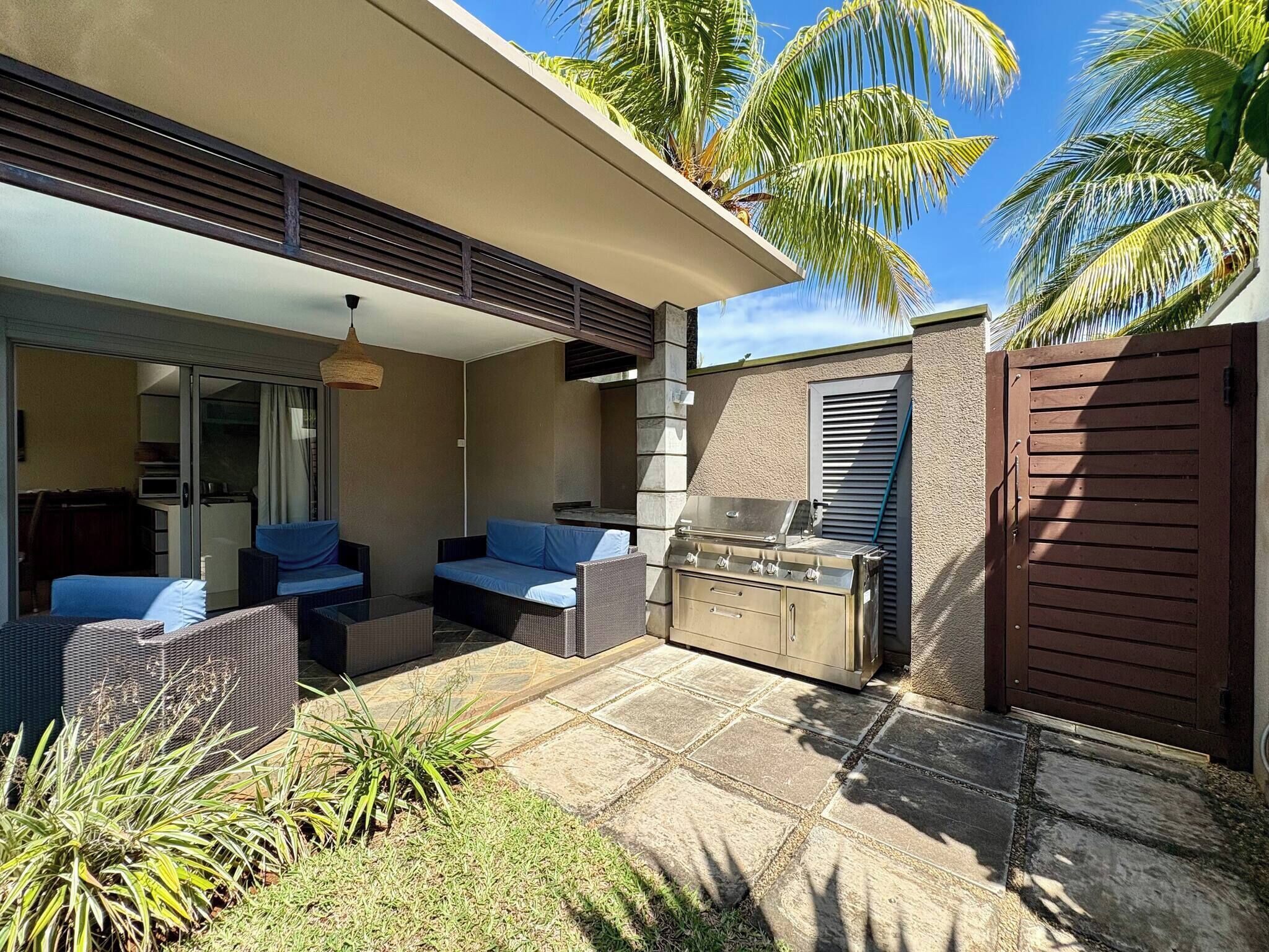An outdoor patio with a grill, seating area, and a sliding glass door leading to a room.