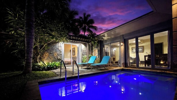 A swimming pool with a glass enclosure, two lounge chairs, and a stone wall with a door leading to an interior space. - Tropical Villa Athena Residence (Grand-Baie)