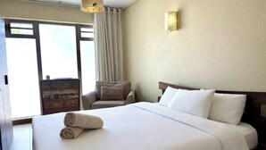A hotel room with a large bed, a chair, a lamp, and a view through a window. - Tropical Villa Athena Residence (Grand-Baie)
